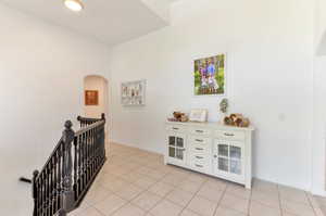 Hall featuring an upstairs landing, light tile patterned flooring, baseboards, and arched walkways