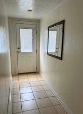 Doorway to outside patio/terrace featuring  tile patterned flooring, a textured ceiling, and baseboards