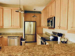 Kitchen featuring maple cabinetry, stainless steel appliances, granite countertops, and pendant lighting