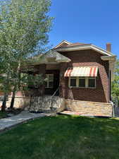 View of front  with a chimney, brick siding, stone stairs, and stone walkway