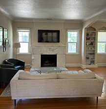 Living area with wood finished floors, a textured ceiling, a fireplace, arched walkways, and built in shelves