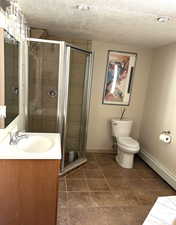 Full bath featuring a baseboard heating unit, vanity, a textured ceiling, and a shower stall