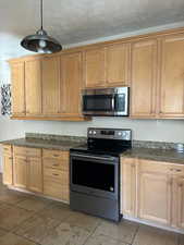 Kitchen with stainless steel appliances, light tile patterned floors, hanging light fixtures, and granite counters