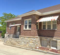 View of side entrance with brick siding, stone siding, awnings, and roof with shingles