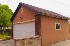View of garage with stucco siding, roof with shingles and stonework
