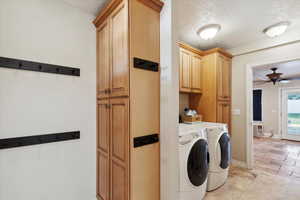 Laundry area featuring washing machine and clothes dryer, cabinet space, a ceiling fan, baseboards, and a textured ceiling