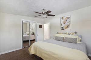 Bedroom with dark colored carpet, baseboards, a closet, a ceiling fan, and a textured ceiling