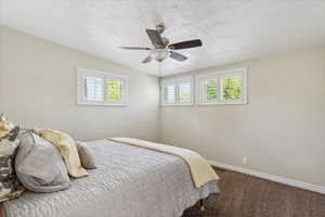 Carpeted bedroom with baseboards, ceiling fan, and a textured ceiling