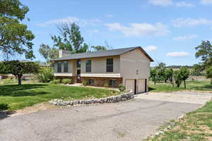 View of front facade featuring a garage, a chimney, a front lawn, driveway, and brick siding