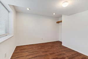 Empty room featuring dark wood-style floors, recessed lighting, baseboards, and a textured ceiling