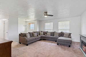 Living area featuring light colored carpet, a textured ceiling, a stone fireplace, a chandelier, and a ceiling fan