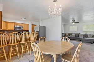 Dining space featuring a ceiling fan, a textured ceiling, light tile patterned floors, and a chandelier