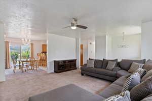 Living area featuring a chandelier, light carpet, a ceiling fan, a textured ceiling, and baseboards