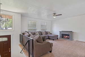 Carpeted living area with a glass covered fireplace, ceiling fan, a textured ceiling, and baseboards