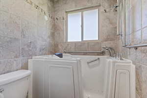 Full bath featuring tile walls, a garden tub, and toilet