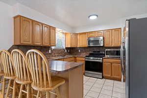 Kitchen with appliances with stainless steel finishes, a sink, a breakfast bar area, a peninsula, and tasteful backsplash