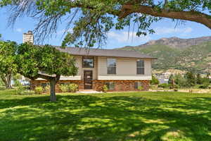 Bi-level home with a front yard, brick siding, a mountain view, and a chimney
