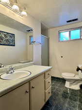 Bathroom with toilet, vanity, a shower stall, a textured ceiling, and tile patterned floors