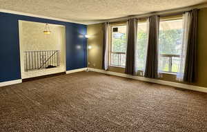 Unfurnished room featuring a textured ceiling, crown molding, carpet, baseboards, and plenty of natural light
