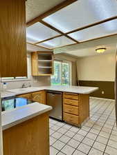 Kitchen featuring dishwasher, a sink, a peninsula, a textured ceiling, and light countertops