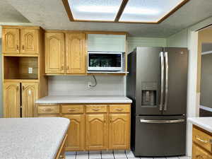Kitchen featuring stainless steel refrigerator with ice dispenser, built in microwave, a textured ceiling, light countertops, and brown cabinets