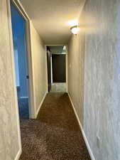 Hall with a textured ceiling, carpet, and baseboards