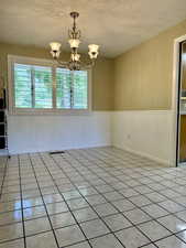 Spare room with a wainscoted wall, a textured ceiling, a chandelier, and light tile patterned flooring