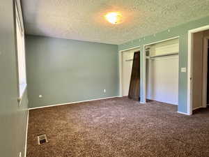 Owners Suite with a textured ceiling, two closets, carpet flooring, and baseboards