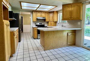 Kitchen with stainless steel appliances, under cabinet range hood, a textured ceiling, a peninsula, and light countertops