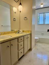 Bathroom featuring double vanity, a textured ceiling, tile patterned floors, toilet, and a bathtub