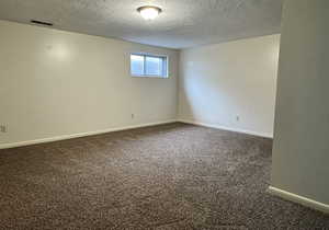 Spare room with a textured ceiling, dark carpet, and baseboards