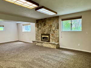 Unfurnished living room featuring carpet, a textured ceiling, a stone fireplace, and baseboards