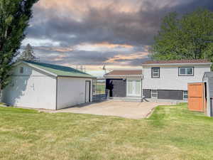 Back of property at dusk featuring french doors, a yard, an outbuilding, and a patio