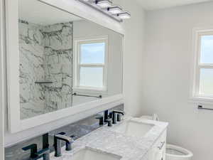 Full bath featuring toilet, double vanity, healthy amount of natural light, and a shower