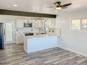 Kitchen with stainless steel appliances, light wood-style floors, decorative backsplash, light countertops, and white cabinets