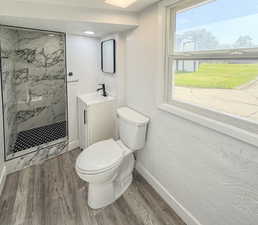 Bathroom featuring wood finished floors, toilet, a marble finish shower, baseboards, and vanity