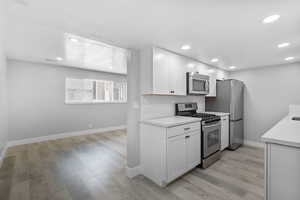Kitchen featuring stainless steel appliances, baseboards, light countertops, white cabinetry, and light wood finished floors