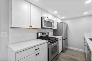 Kitchen with stainless steel appliances, light wood-style flooring, white cabinetry, baseboards, and recessed lighting