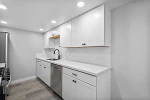 Kitchen with stainless steel appliances, a sink, light wood finished floors, recessed lighting, and white cabinetry