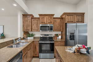 Kitchen with stainless steel appliances, a sink, dark stone countertops, brown cabinets, and recessed lighting