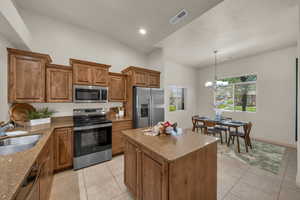 Kitchen featuring appliances with stainless steel finishes, a sink, brown cabinetry, light tile patterned floors, and vaulted ceiling