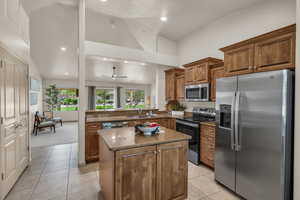 Kitchen featuring appliances with stainless steel finishes, a sink, dark stone counters, a center island, and brown cabinetry