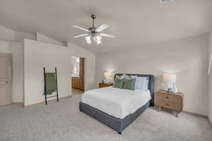 Bedroom featuring lofted ceiling, baseboards, a ceiling fan, ensuite bath, and light carpet