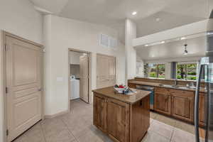 Kitchen with washer / dryer, a sink, stainless steel dishwasher, a kitchen island, and brown cabinetry