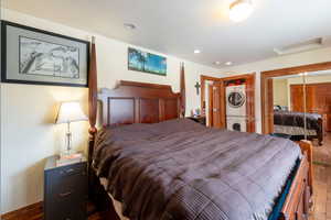 Bedroom with estacked washer and dryer, attic access, hardwood / wood-style floors, a closet, and recessed lighting