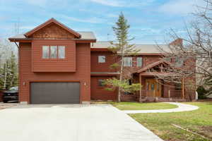 Rustic home with driveway, an attached garage, a front lawn, roof with shingles, and covered porch