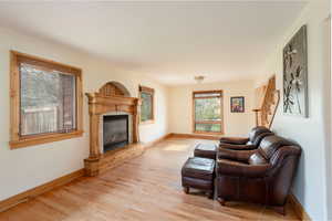 Living room featuring light wood-type flooring, a glass covered fireplace, baseboards, and stairway