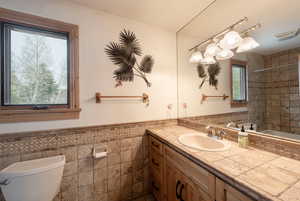 Bathroom with tile walls, toilet, vanity, and a wainscoted wall