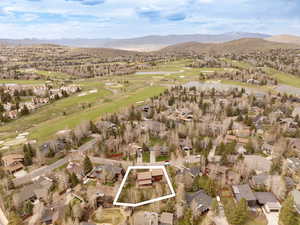 Aerial view of property's location with property boundaries highlighted, a golf course, nearby suburban area, and a water and mountain view