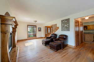 Living area with a fireplace with raised hearth, light wood-style flooring, baseboards, and stairs